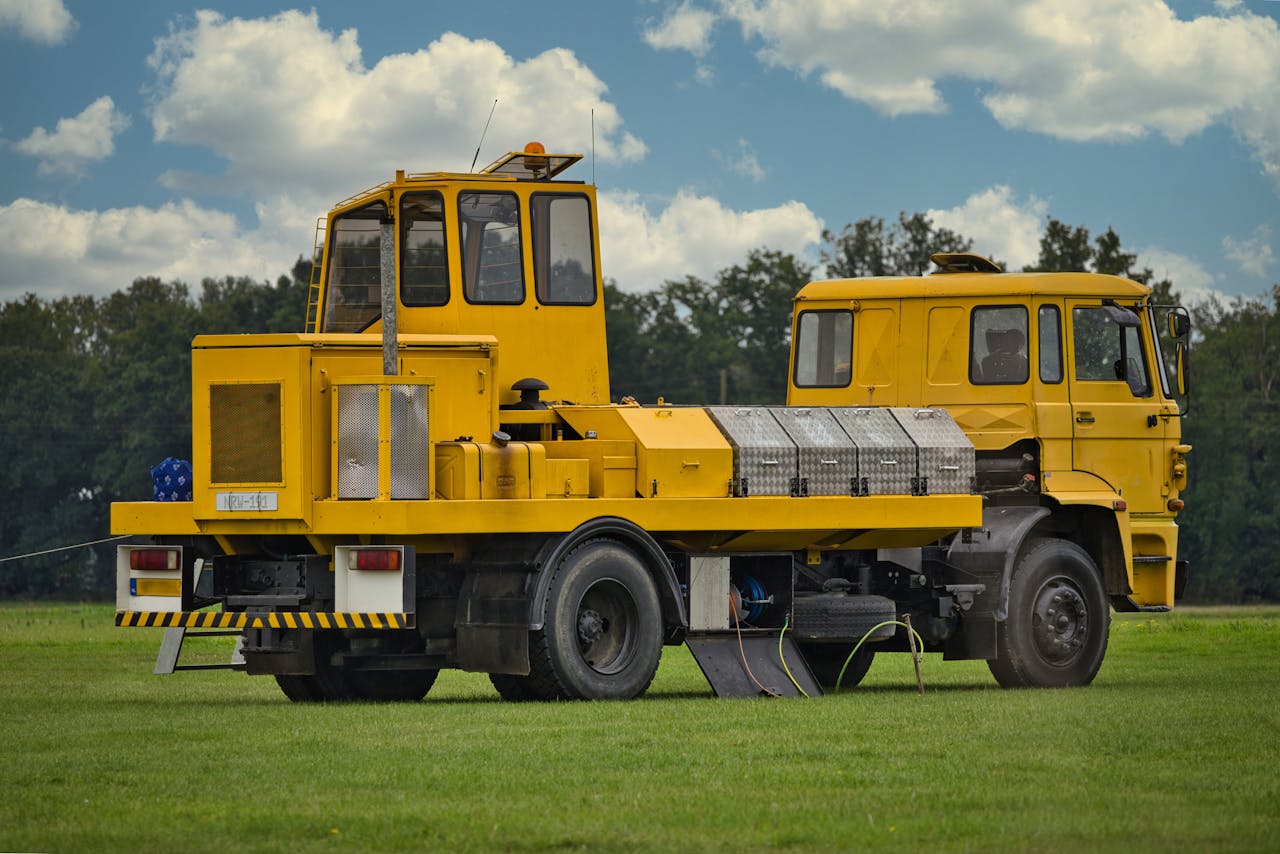 A yellow commercial vehicle parked on a grassy field under a cloudy blue sky.